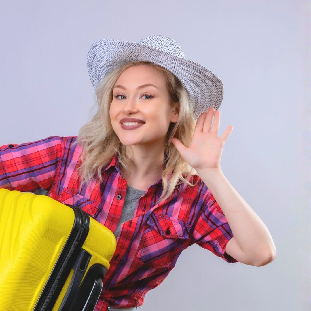 Smiling woman holding a suitcase and cupping her hand to her ear to listen to aviation news.